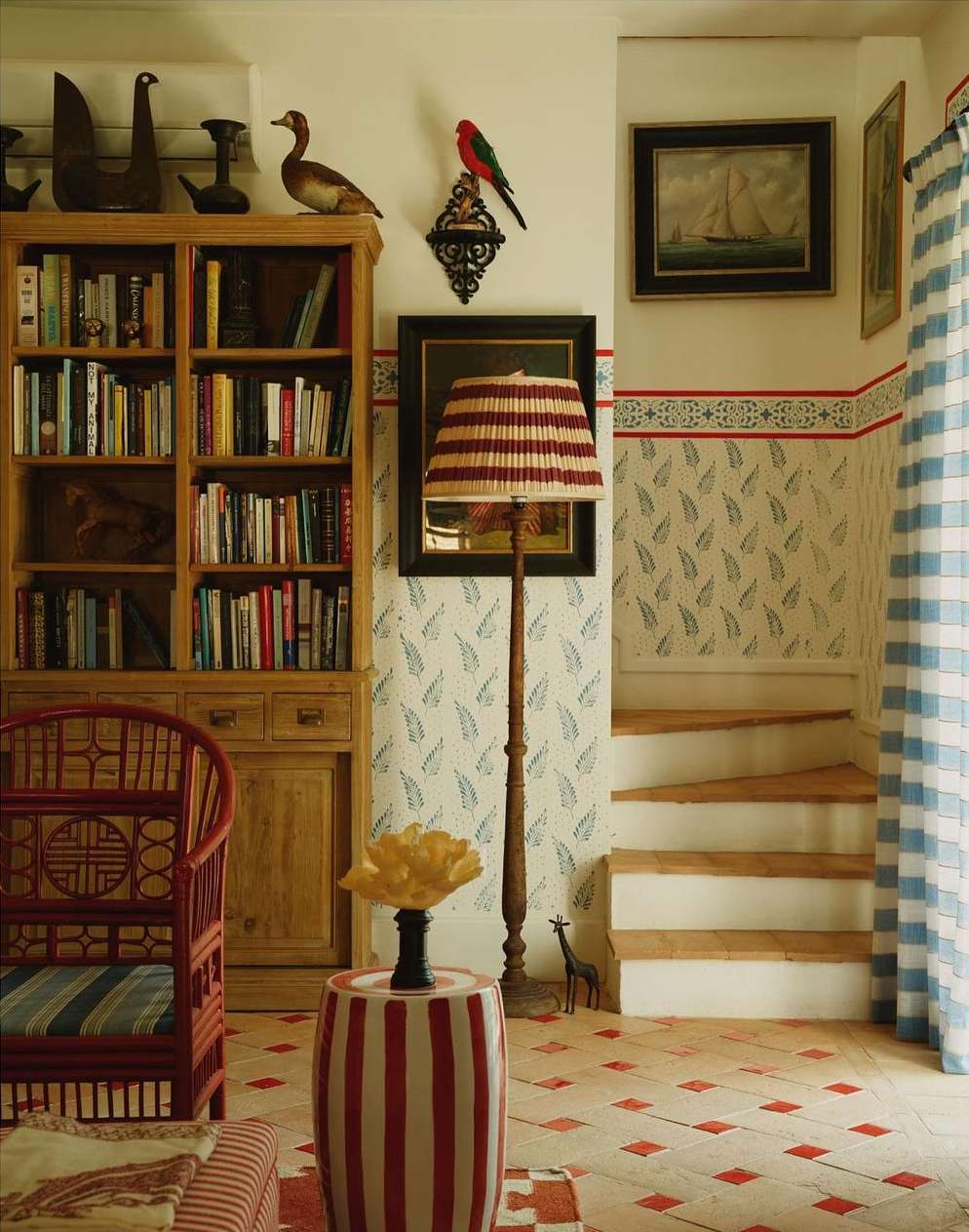 Interior of a cozy room with a bookcase, colorful decor, floral wallpaper, and an inviting staircase, creating a warm and artistic space.