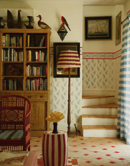 Interior of a cozy room with a bookcase, colorful decor, floral wallpaper, and an inviting staircase, creating a warm and artistic space.