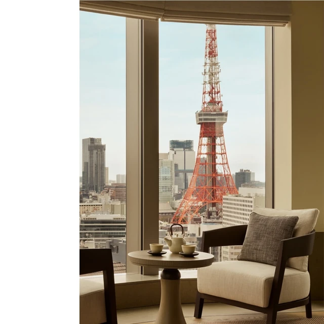 Interior view of a neutral toned living area with a circular table set for tea, a chair, and a large window with city views.