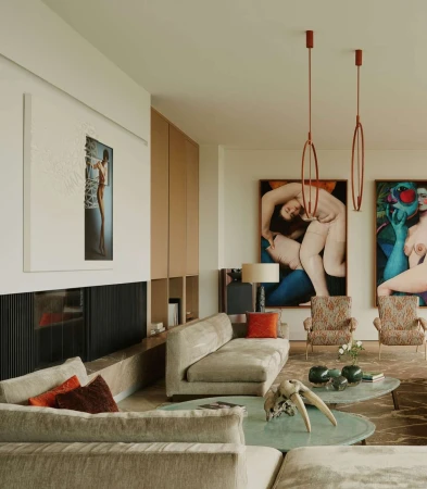 Living room interior with grey sofas, contemporary art, and patterned armchairs in a light-filled space, complemented by modern lighting.