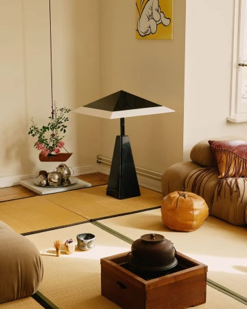Interior view showcasing a black table lamp, tatami mat flooring, tea ceremony set, and artwork in a naturally lit room.