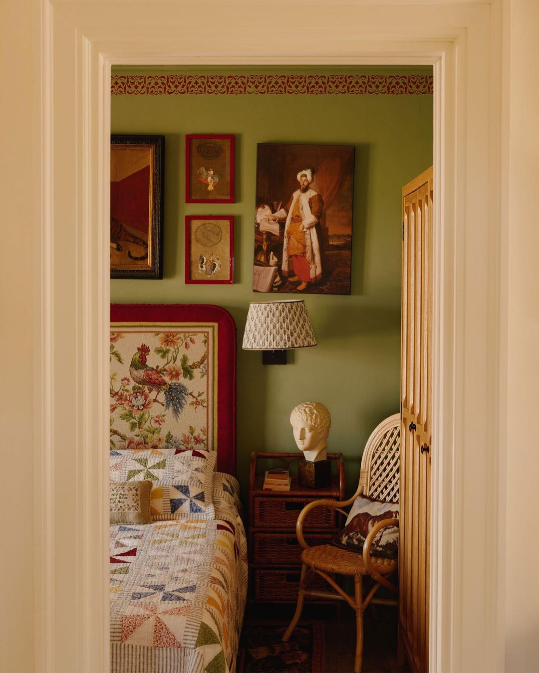 Eclectic bedroom interior featuring a patchwork quilt, floral headboard, and antique decor, viewed through a doorway, creating a cozy and inviting space.