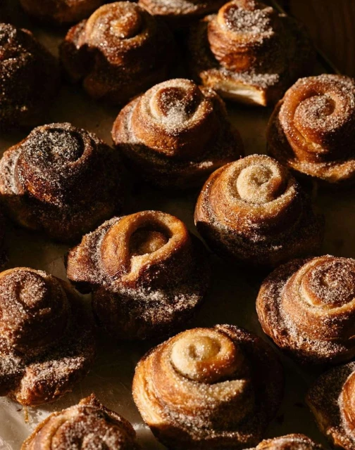 Close-up of freshly baked cinnamon rolls, topped with sugar, showcasing their swirl pattern and golden-brown color in warm lighting.