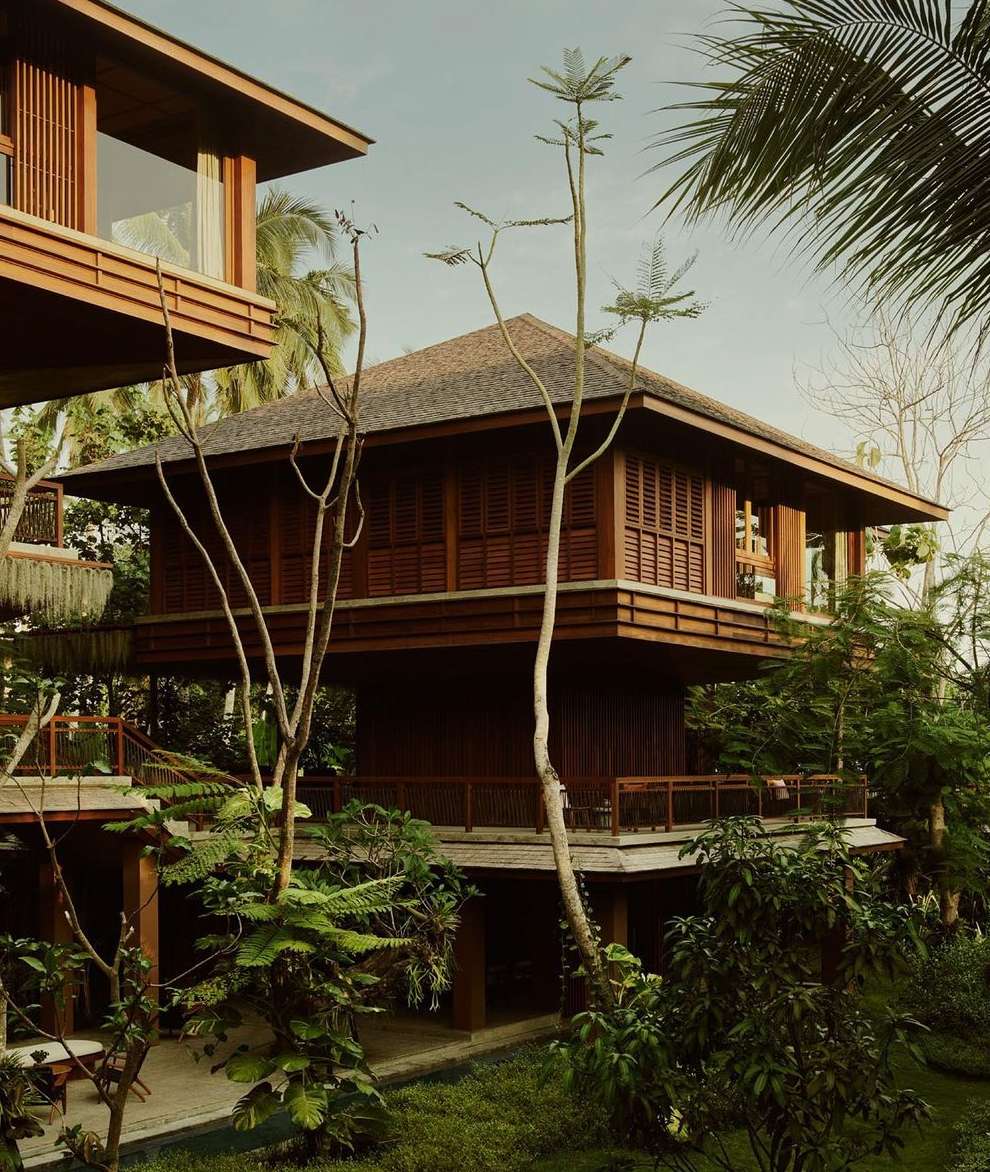 Elevated timber house amidst lush greenery and trees, showcasing sustainable architecture and tropical living in an outdoor environment.