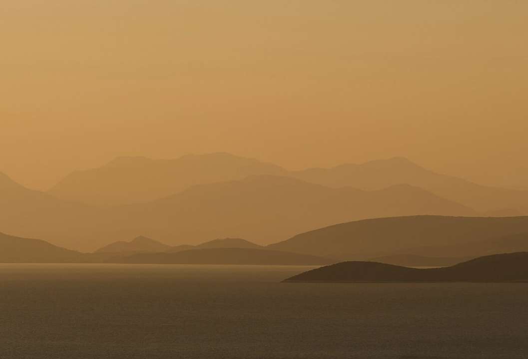 Scenic view of a calm body of water reflecting the warm, golden light of the sky, with layered, silhouetted hills in the background.