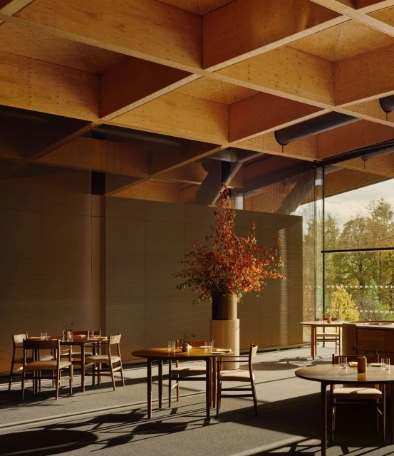 Warm-toned interior of a dining room with round tables and wood chairs, natural light streams through large windows showcasing green trees outside.