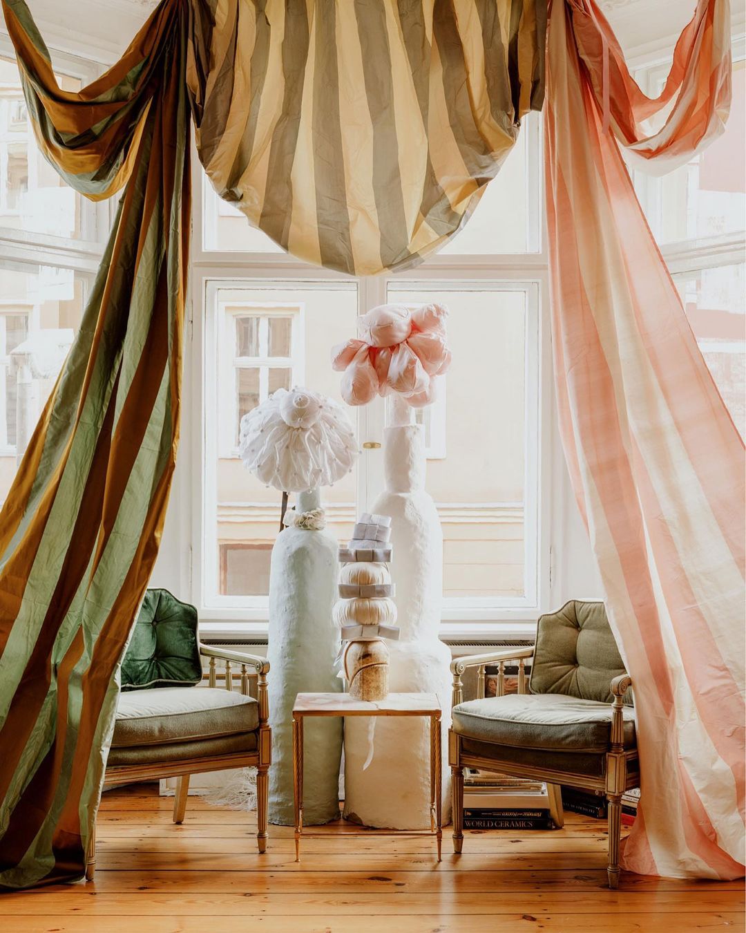 Interior scene featuring vintage chairs, striped curtains, decorative vases, and a small marble-topped table in a room with a window view.