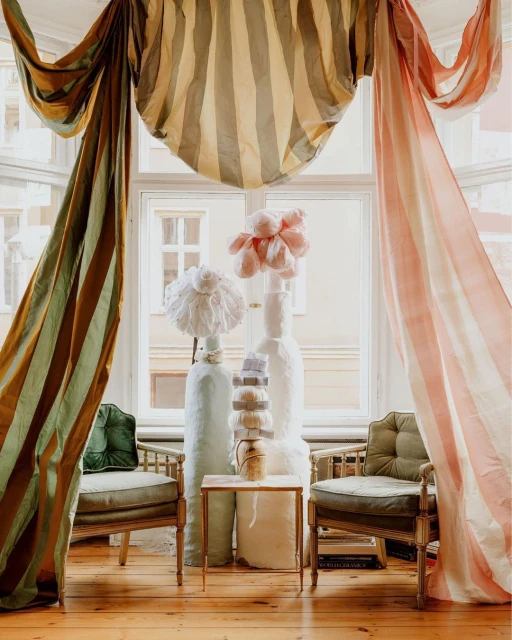 Interior scene featuring vintage chairs, striped curtains, decorative vases, and a small marble-topped table in a room with a window view.