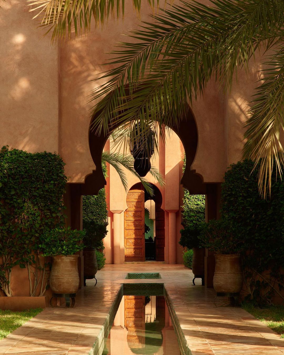 Outdoor architecture with Moorish archway, reflecting pool, and palm trees create tranquil Moroccan courtyard garden design.