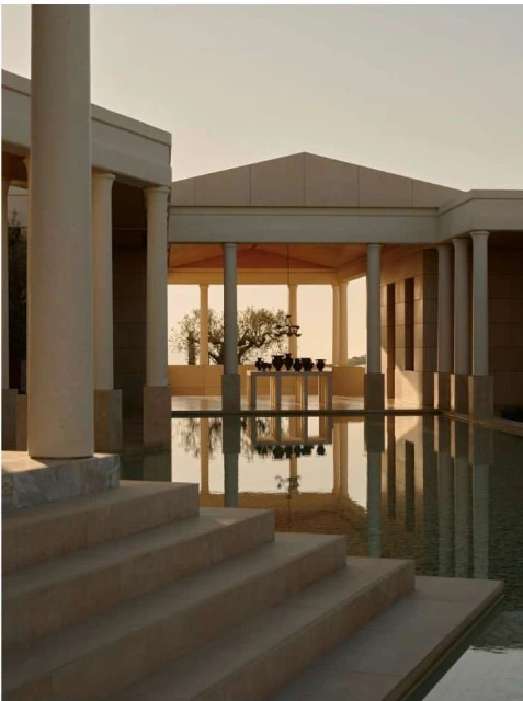 Exterior shot of modern architecture featuring columns, a reflecting pool, and a building in beige tones during the daytime.