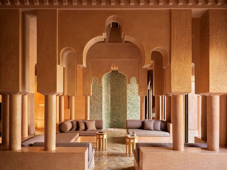 Warmly lit Moroccan-style interior featuring arched columns, recessed seating with cushions, and decorative tile work.