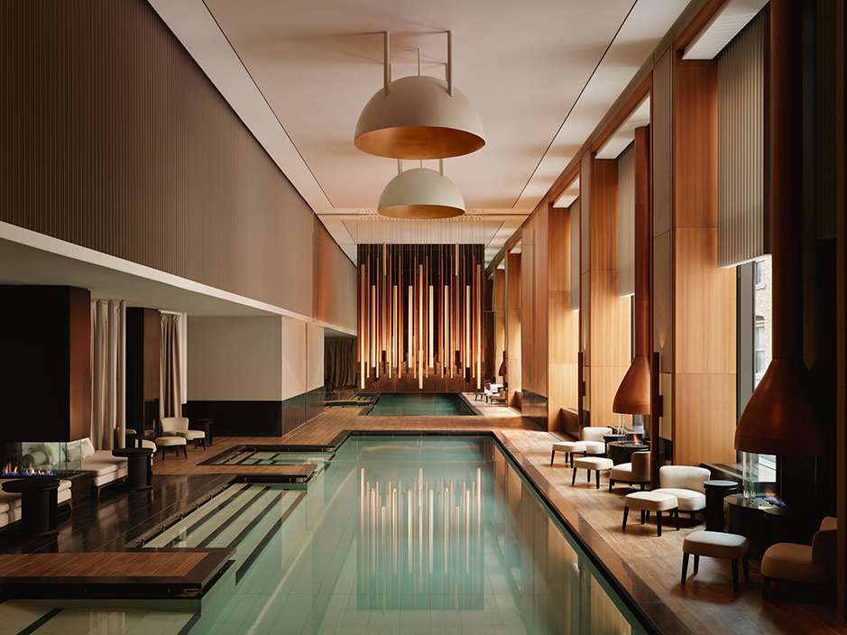 Indoor swimming pool area with elegant recessed lighting, wood paneling, lounge seating, and serene water reflections in a luxury spa.