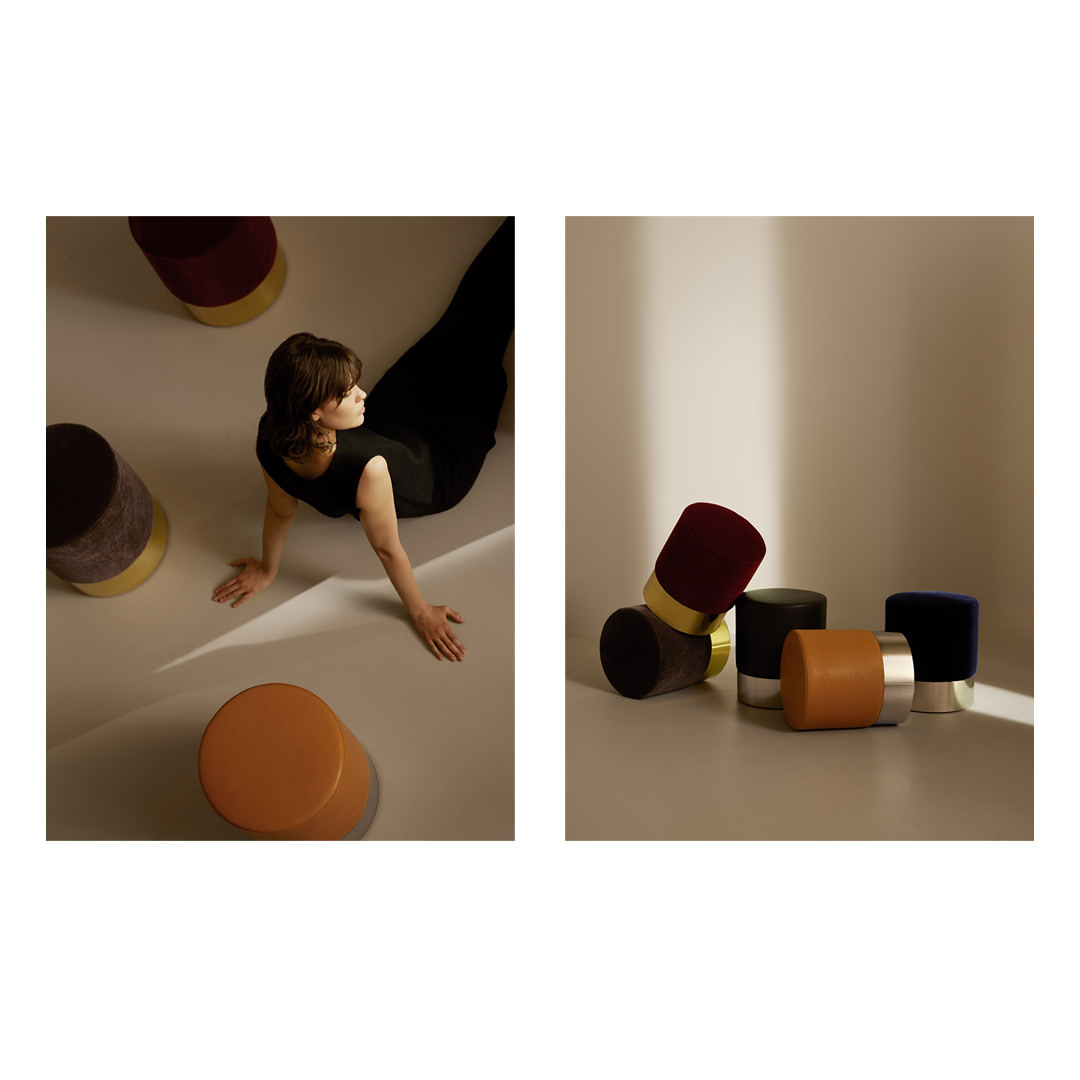 Woman sitting on floor near multicolored velvet stools. Image shows stool collection featuring cylindrical design with gold and silver bases.