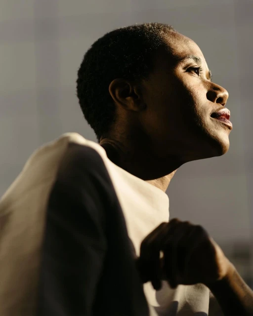 Portrait of an African-American woman looking up. The background is blurred, with natural light and shadows creating a textured effect.