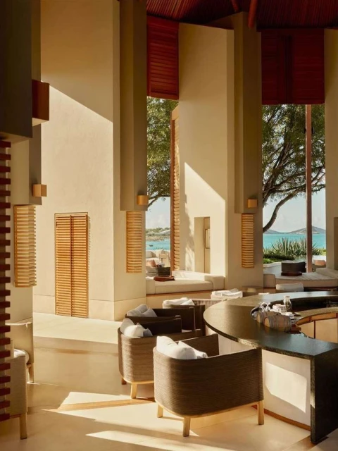 Interior view of a hotel lobby with light wood columns, window seating, and rattan furniture creating a relaxing environment.
