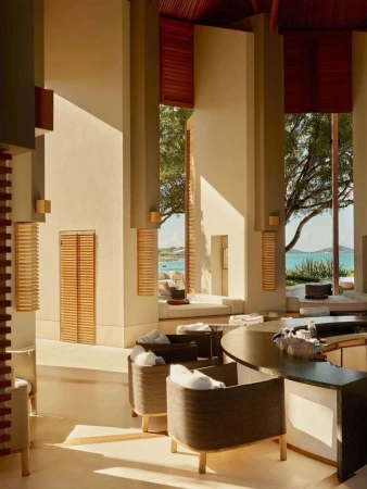 Interior view of a hotel lobby with light wood columns, window seating, and rattan furniture creating a relaxing environment.