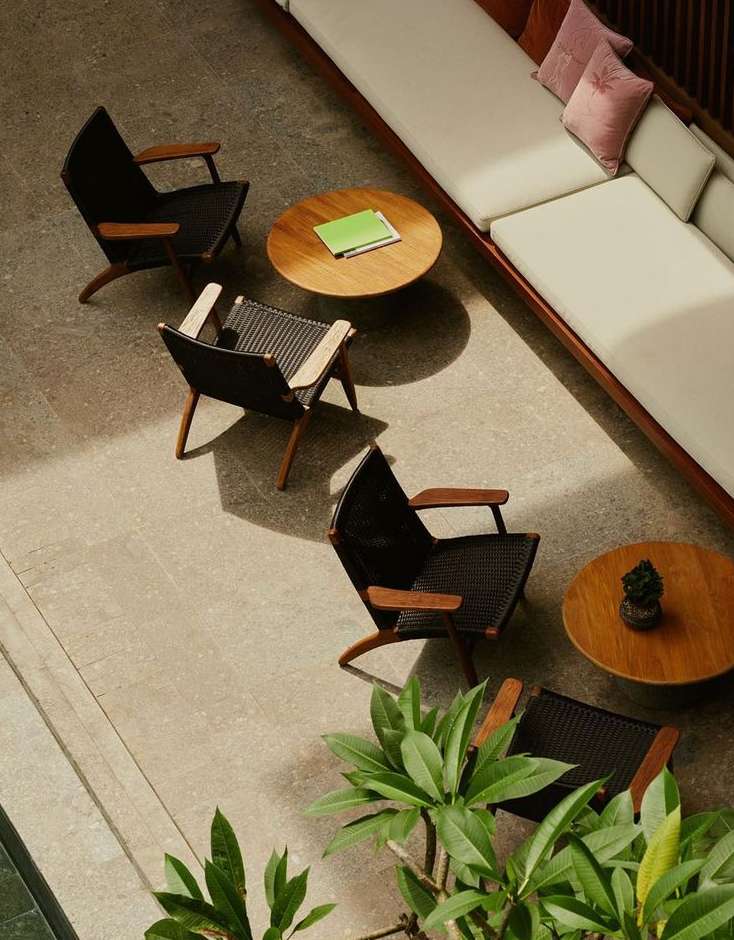 Interior design featuring black wicker chairs with wooden frames arranged around two wood tables and a long white sofa with pillows.