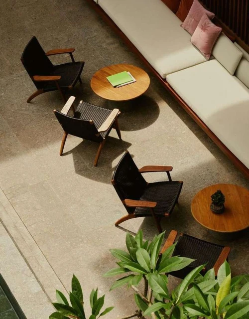 Interior design featuring black wicker chairs with wooden frames arranged around two wood tables and a long white sofa with pillows.