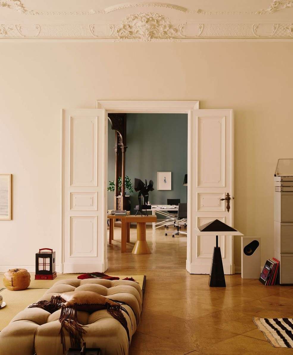 Interior view of a living room with a tufted couch on a parquet floor, open doorways, vintage furniture, and modern decor.