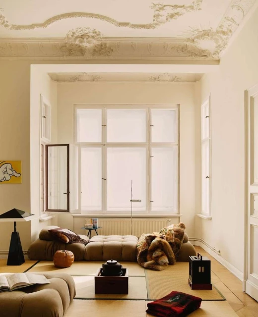 Living room interior featuring a tufted sofa, decorative objects, and natural light streaming through a large window, creating a cozy atmosphere.