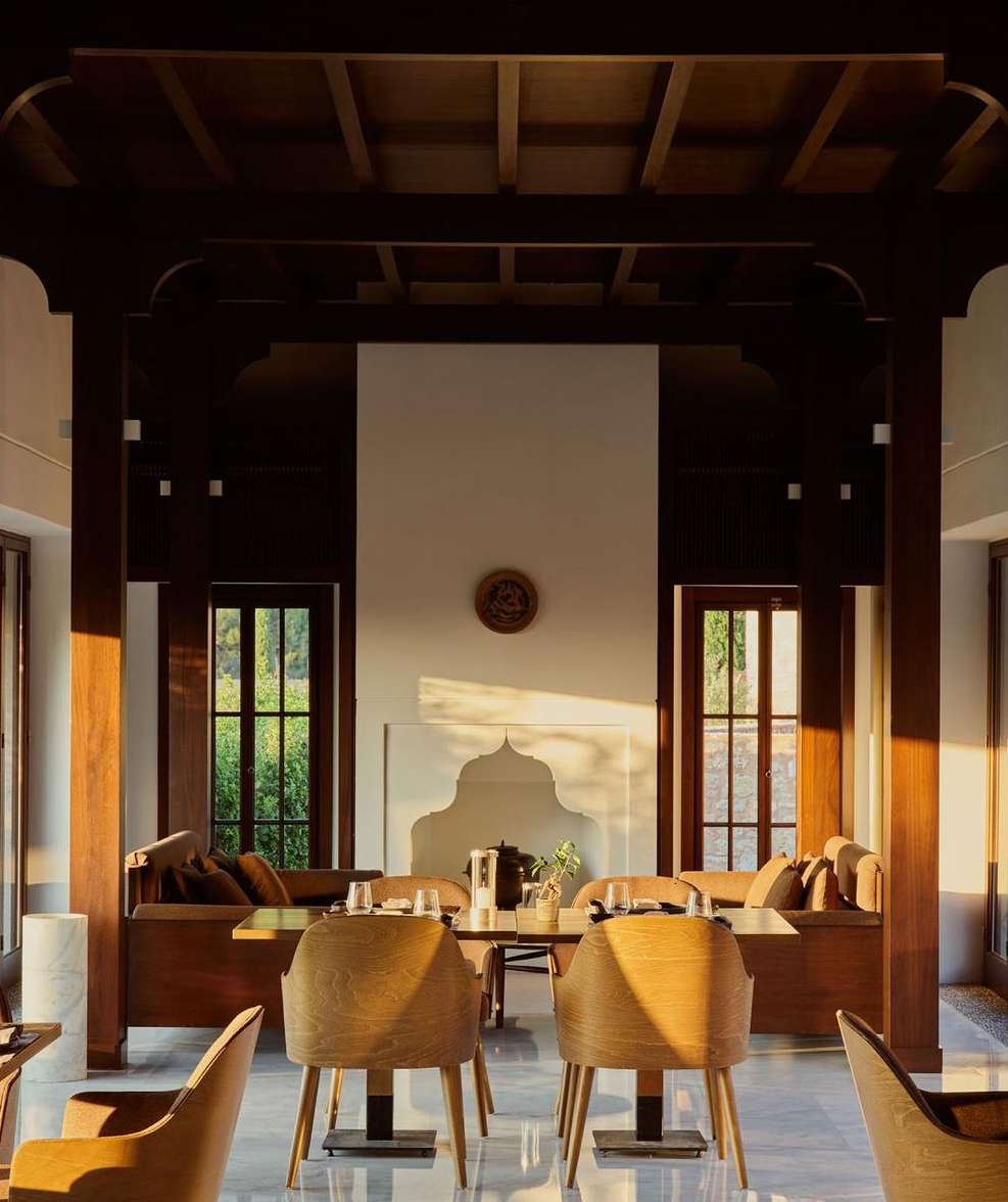 Dining room interior featuring wooden chairs, a table setting, and warm sunlight streaming through windows, creating a cozy atmosphere.