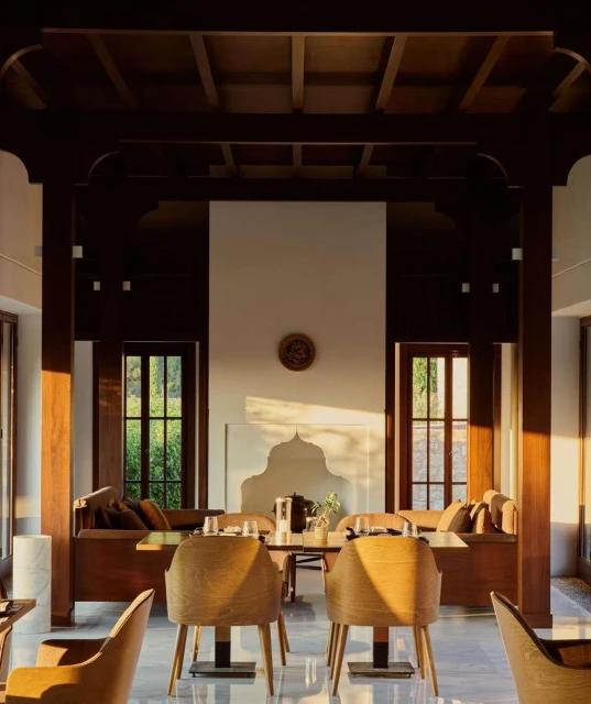 Dining room interior featuring wooden chairs, a table setting, and warm sunlight streaming through windows, creating a cozy atmosphere.