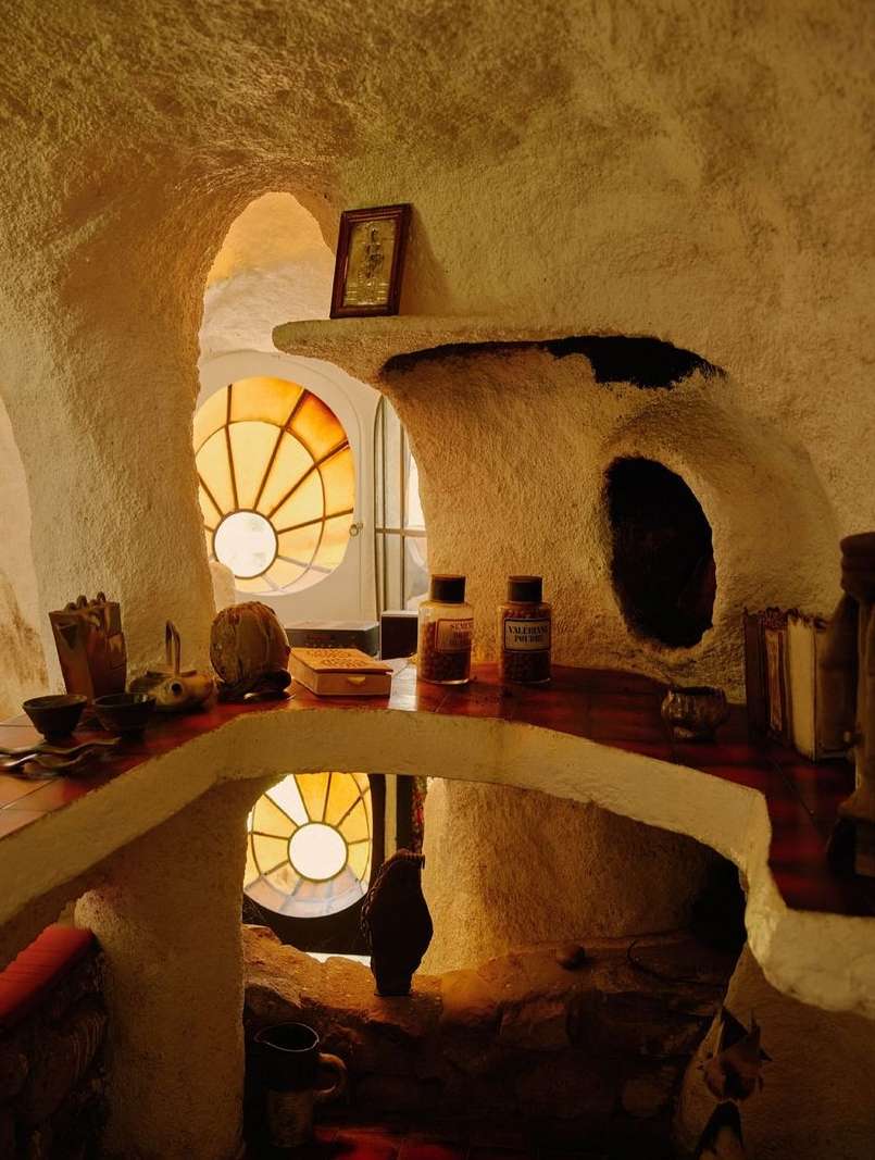 Interior view of a uniquely designed room with textured walls, stained glass window, shelves displaying decorative objects and containers.