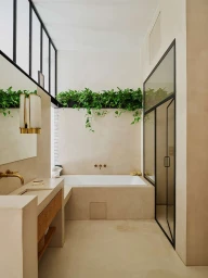 Modern minimalist bathroom interior with built-in bathtub, concrete vanity, and trailing green houseplants.