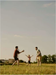 Three people playing catch with a ball in a grassy park under a clear sky during the day.