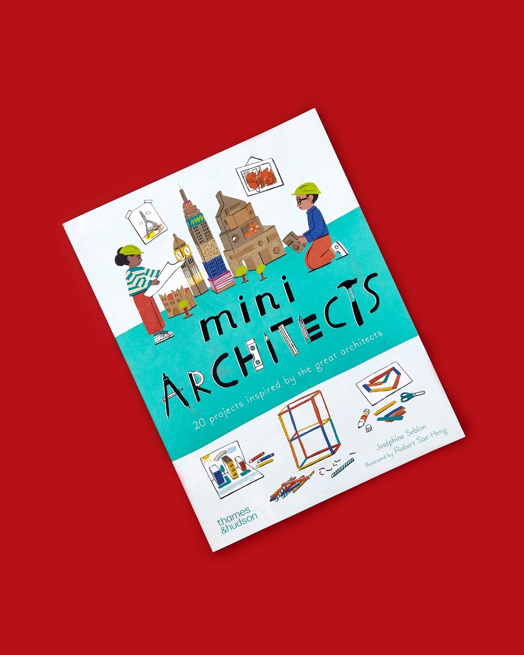 A children's architecture book, titled 'mini ARCHITECTS', lies on a red background, featuring colorful cartoon illustrations of buildings.