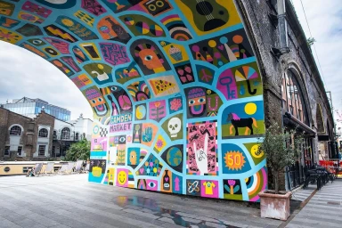 Vibrant colourful mural with diverse icons painted underneath a railway bridge archway in London by Robert Sae-heng.