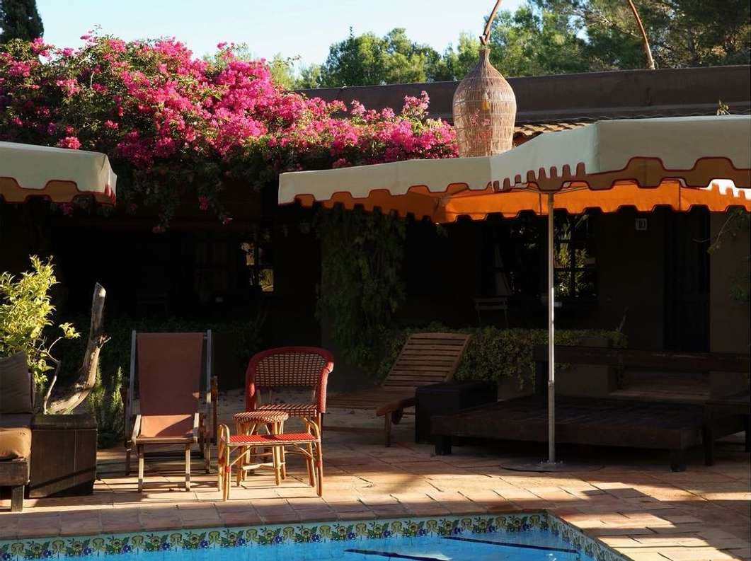 Outdoor patio with lounge chairs, tables, umbrella, and pool. Pink bougainvillea on the roof and an ornamental vase on the patio.