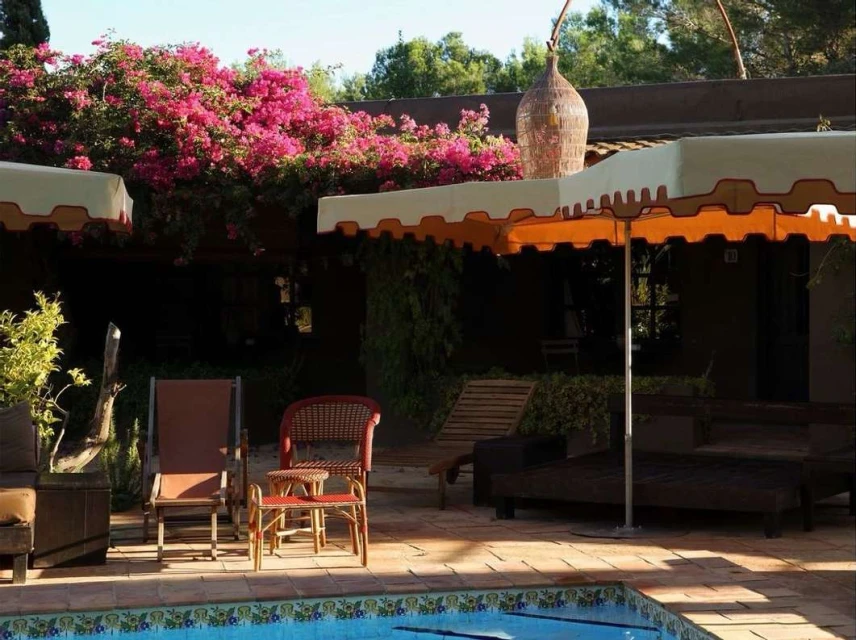 Outdoor patio with lounge chairs, tables, umbrella, and pool. Pink bougainvillea on the roof and an ornamental vase on the patio.