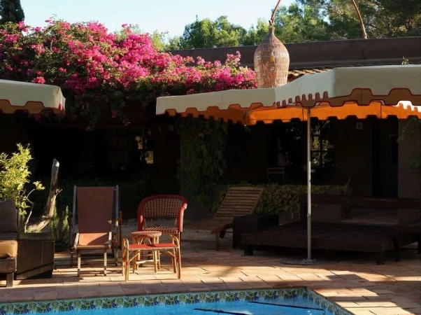 Outdoor patio with lounge chairs, tables, umbrella, and pool. Pink bougainvillea on the roof and an ornamental vase on the patio.