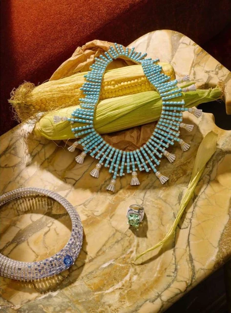 Three jewelry items including a necklace, ring, and choker displayed with corn cobs on a mottled marble surface, top-down studio shot.