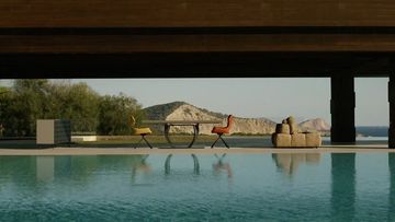 Outdoor living space with swimming pool overlooking the ocean and mountain, featuring modern outdoor furniture on the patio.