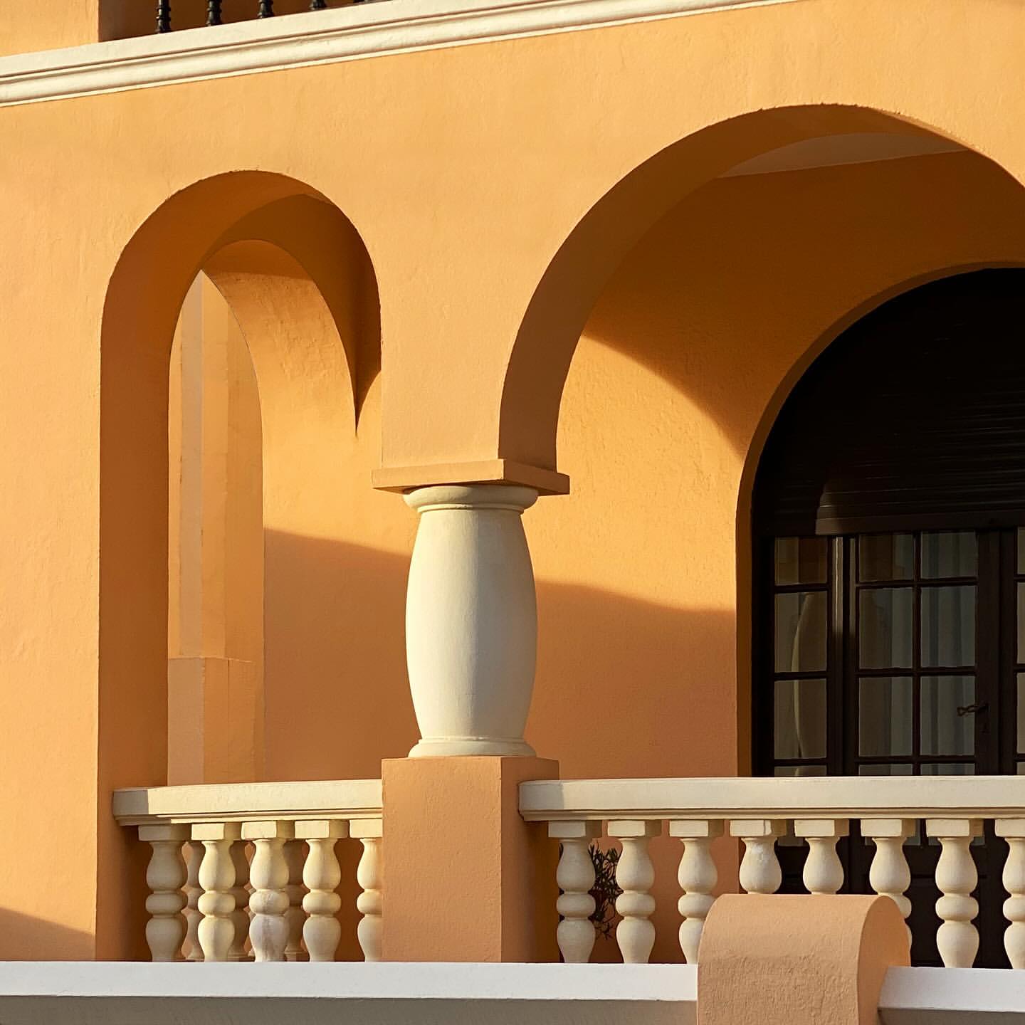 Architectural detail of a peach-colored building featuring arched openings, a white balustrade, and a glimpse of a dark window.