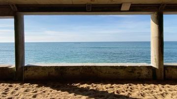 Seascape view of ocean through concrete structure with sand in foreground. Clear blue skies and sea, peaceful, calming coastal scene.
