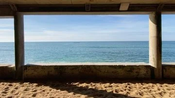 Seascape view of ocean through concrete structure with sand in foreground. Clear blue skies and sea, peaceful, calming coastal scene.