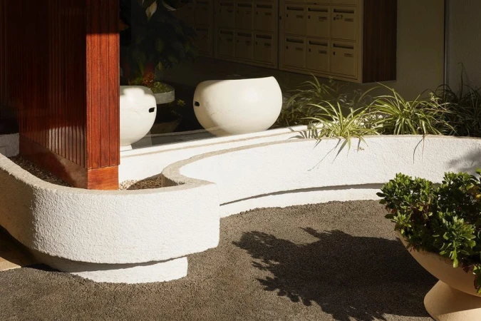 Outdoor space features textured white planters, green foliage, and mailbox units in neutral colors, creating a serene architectural scene.