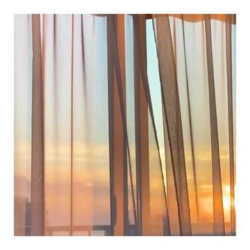 Abstract view of a window with sheer curtains during sunrise or sunset, showing warm orange sunlight and bright sky.