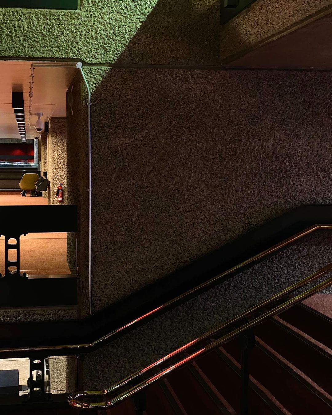 Interior architecture shot featuring a stairway with a brass railing and a concrete wall in a dimly lit indoor setting during the evening.