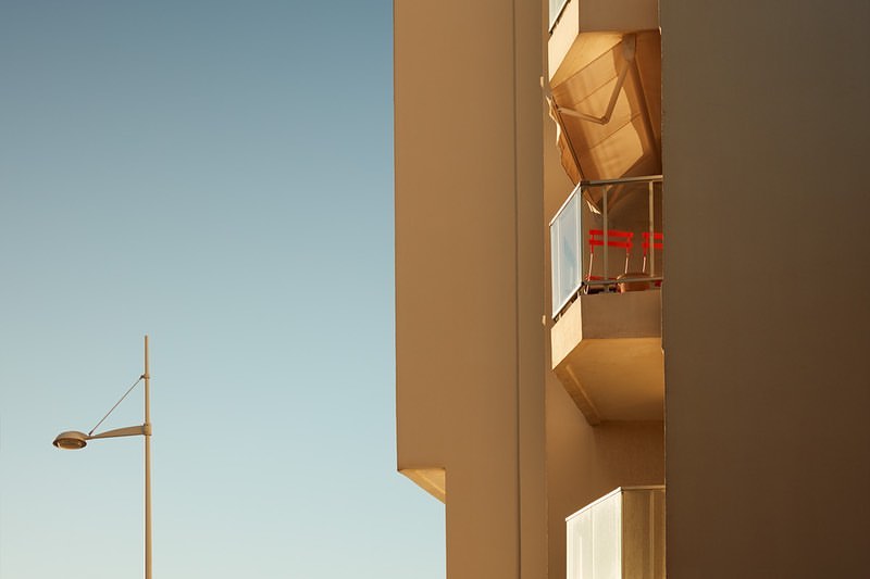 Modern architecture showcases a building with a balcony under clear blue skies, complemented by a vintage street lamp.