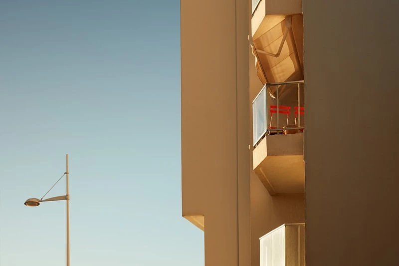 Modern architecture showcases a building with a balcony under clear blue skies, complemented by a vintage street lamp.