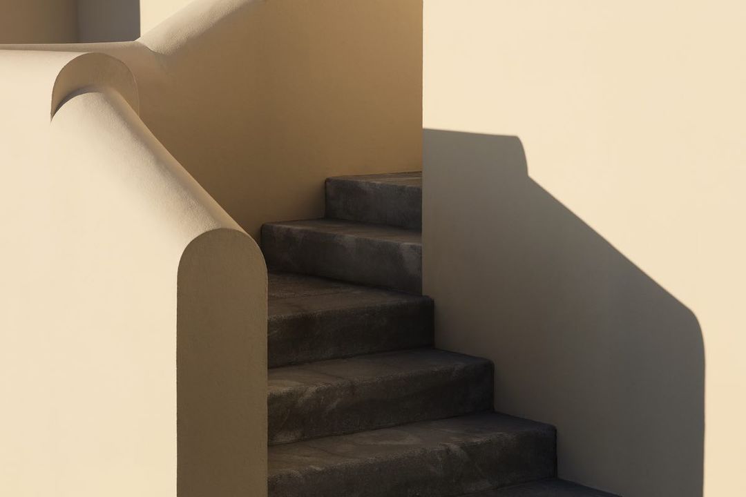 Architectural photograph showcases a staircase with cream-colored walls, strong shadows, and a minimalist design, emphasizing clean lines and form.