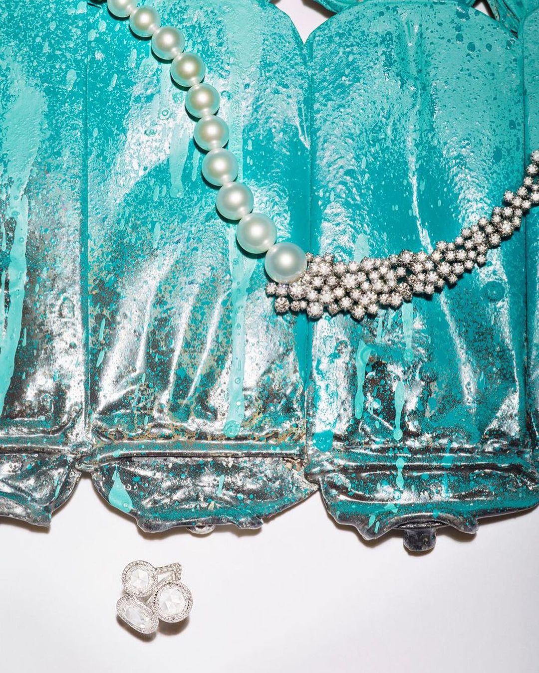 Elegant pearl necklace and diamond jewelry displayed against a textured teal and gray backdrop in a visually appealing still life.
