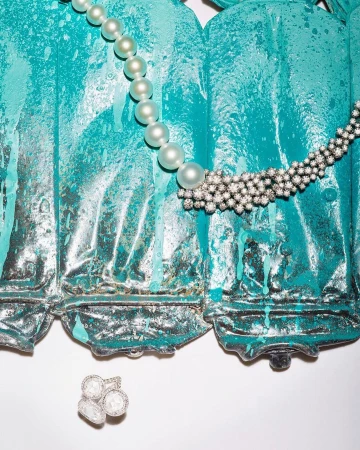 Elegant pearl necklace and diamond jewelry displayed against a textured teal and gray backdrop in a visually appealing still life.