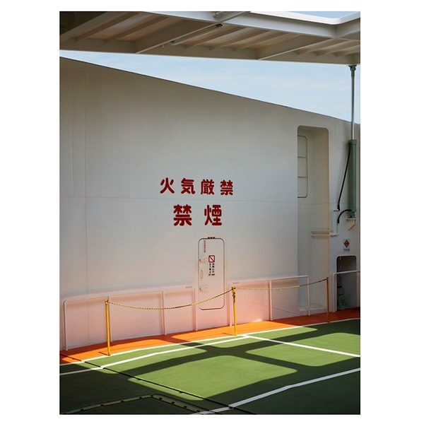 White wall with a red 'No Smoking' sign in Japanese and a small door with a no smoking symbol, over a green and orange floor.