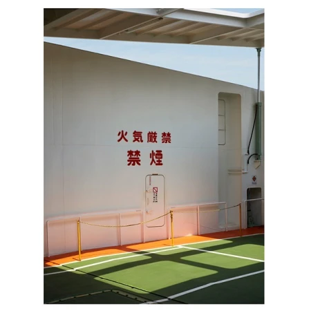 White wall with a red 'No Smoking' sign in Japanese and a small door with a no smoking symbol, over a green and orange floor.