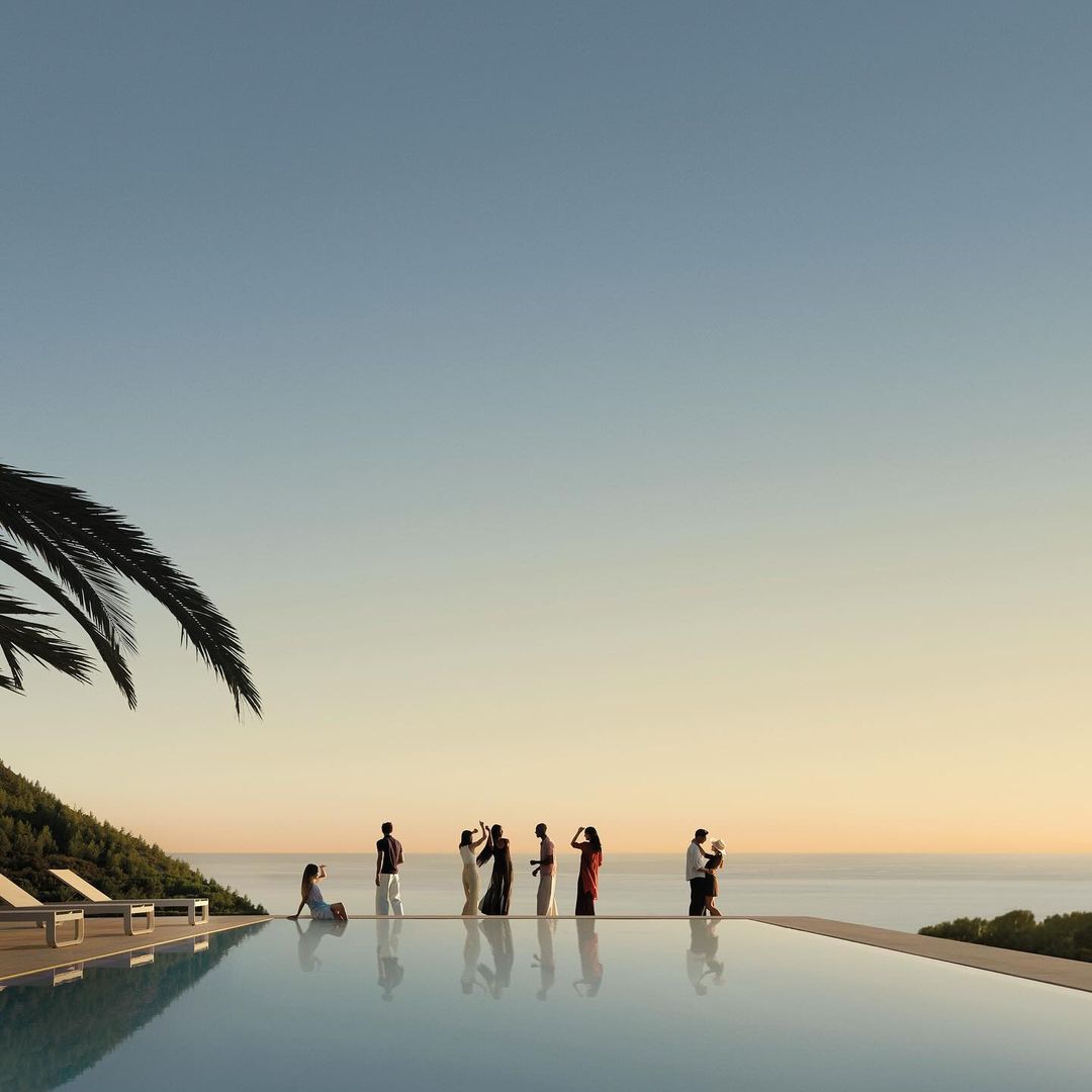 Group of people standing by an infinity pool with the ocean in the background at sunset. Palm tree to the left of the frame.